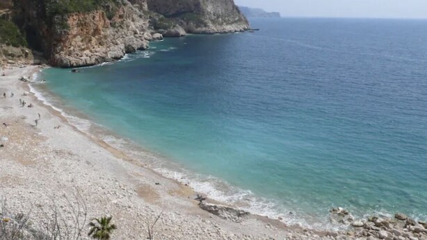Une plage côtière bordée de falaises rocheuses et baignée d’eaux d’un bleu limpide.