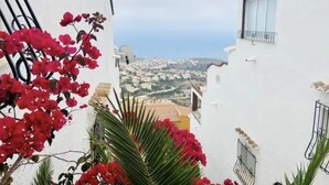 Une rue étroite bordée de bâtiments blancs, avec une vue sur la mer et des fleurs rouges au premier plan.
