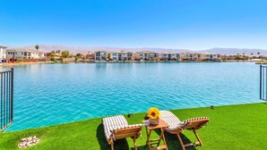 A poolside area with a table and two chairs, a flower vase, and a view of a row of buildings across a body of water. - Lakefront with privet Pool 4 master  (Indio)