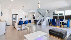 A spacious living area with a kitchen, a dining area with blue chairs, a staircase, and a large window. - Lakefront with privet Pool 4 master  (Indio)
