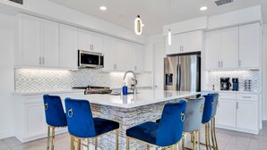 A modern kitchen with white cabinets, a marble island, and blue bar stools. - Lakefront with privet Pool 4 master  (Indio)