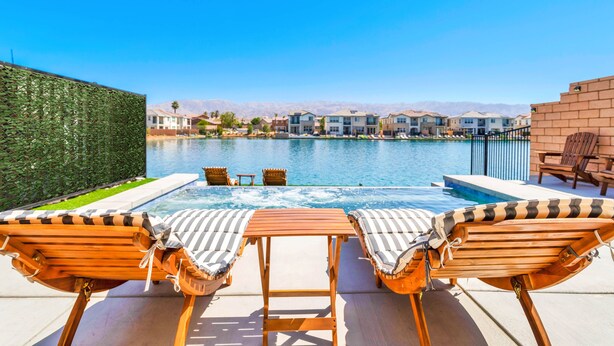 A poolside area with lounge chairs and a table, a clear view of the pool, and a backdrop of residential buildings. - Lakefront with privet Pool 4 master  (Indio)