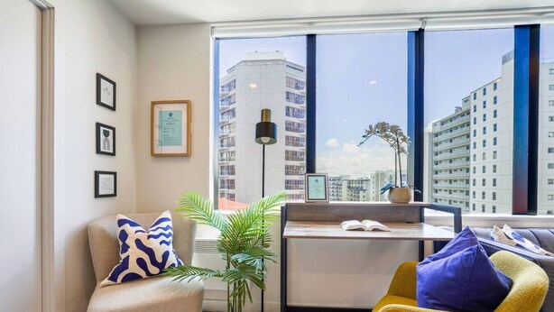 A modern living room with a sofa, a yellow chair, a small table, and a large window with a city view. - Two Bedroom Apartment Right Next to the Sky Tower (Auckland)