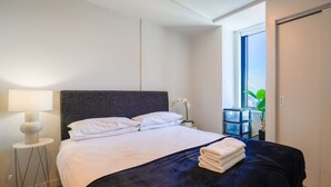 A hotel room with a bed, a nightstand, a lamp, and a view of the outdoors. - Two Bedroom Apartment Right Next to the Sky Tower (Auckland)
