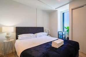A hotel room with a bed, a nightstand, a lamp, and a view of the outdoors.