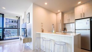 A modern kitchen with a bar area, a dining table with chairs, and a view of the city through large windows. - Two Bedroom Apartment Right Next to the Sky Tower (Auckland)