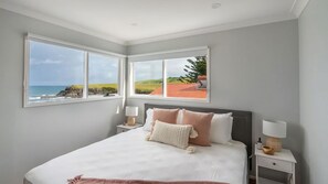 Ein Schlafzimmer mit einem großen Bett, zwei Nachttischen und Meerblick durch große Fenster.
