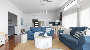 Ein modernes Wohnzimmer mit einem blauen Sofa, einem runden Couchtisch und einem Essbereich im Hintergrund.