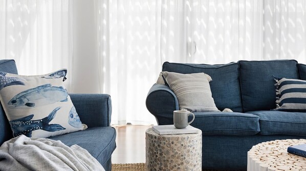 Un salon avec un canapé bleu, un coussin à motifs, une petite table d’appoint et une table basse ronde en bois.