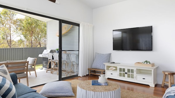 A modern living room with a TV, a sofa, a dining area with chairs, and a sliding glass door leading to an outdoor space.