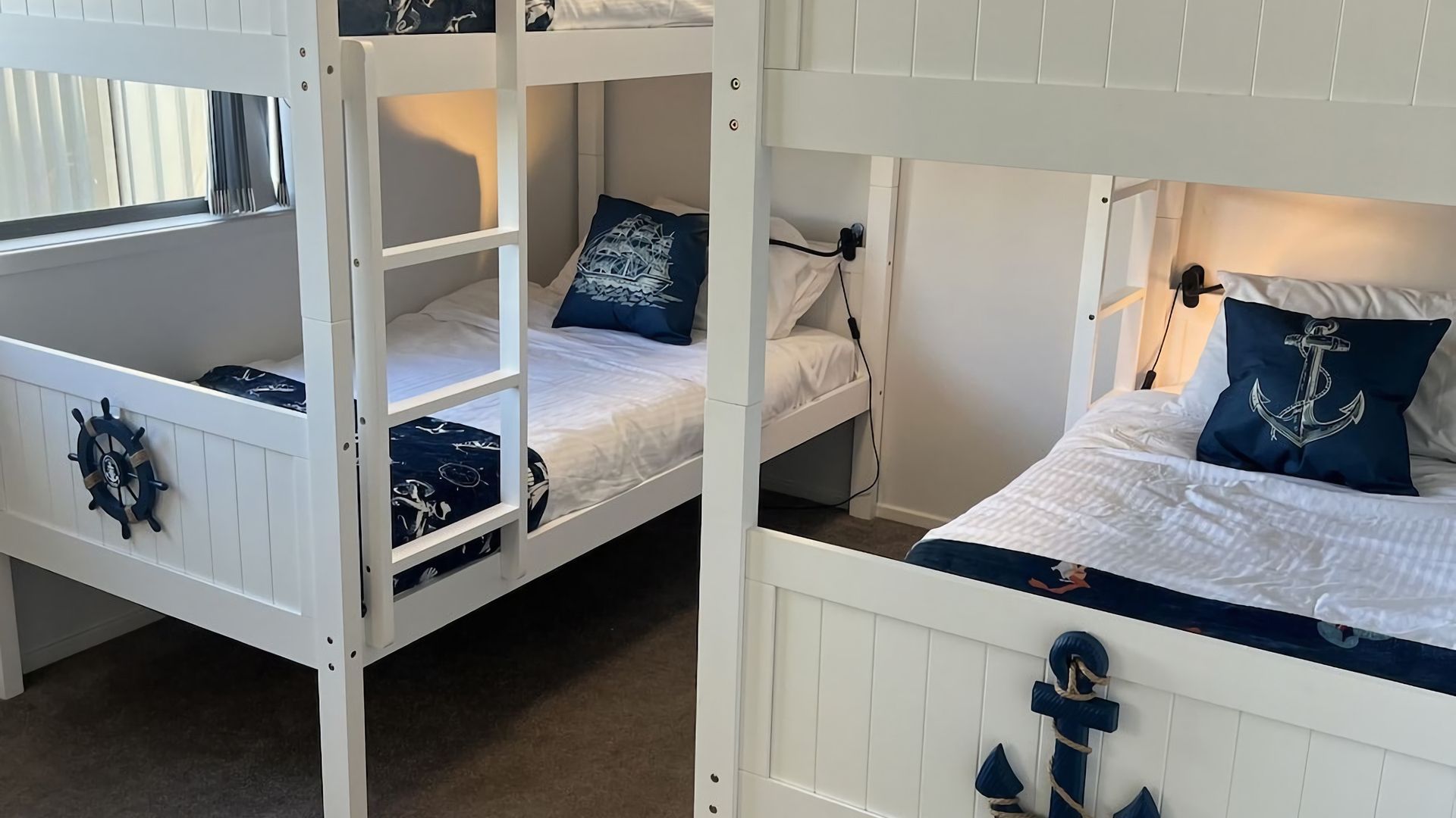 Une chambre avec des lits superposés décorée sur le thème de la marine, avec notamment un décor représentant un gouvernail de navire et un coussin en forme d’ancre.