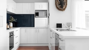 A modern kitchen with white cabinetry, a microwave, a coffee machine, and a sink. - Seagrass a family beach house (Vincentia)