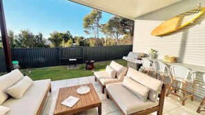 Eine Terrasse im Freien mit einer Sofagarnitur, einem Holztisch und einem Grillbereich.