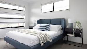 A modern bedroom with a bed, nightstands, and a window.