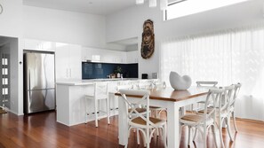 Une cuisine moderne avec des meubles blancs, un réfrigérateur en acier inoxydable et un coin repas comprenant des chaises blanches et une table en bois.