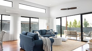 A spacious living area with a blue sofa set, a coffee table, and a view of the outdoors through large sliding glass doors. - Seagrass a family beach house (Vincentia)
