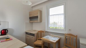 A compact kitchen with a window, wooden cabinets, a red kettle, and a table with chairs. - Spreewald-Familienherberge (Lübbenau/Spreewald)