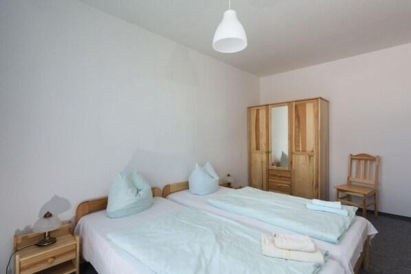 Un dormitorio con dos camas, un armario de madera, una silla y una mesita de noche con lámpara.