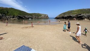 Une plage de sable où l’on voit des gens, avec des collines rocheuses en arrière-plan.