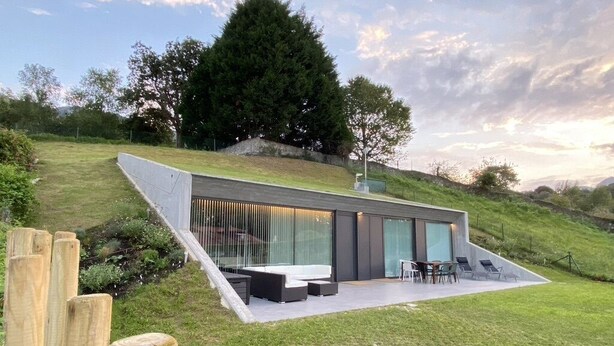 Une maison moderne avec un toit en pente, une terrasse dotée de mobilier d’extérieur et une vue sur le paysage environnant.