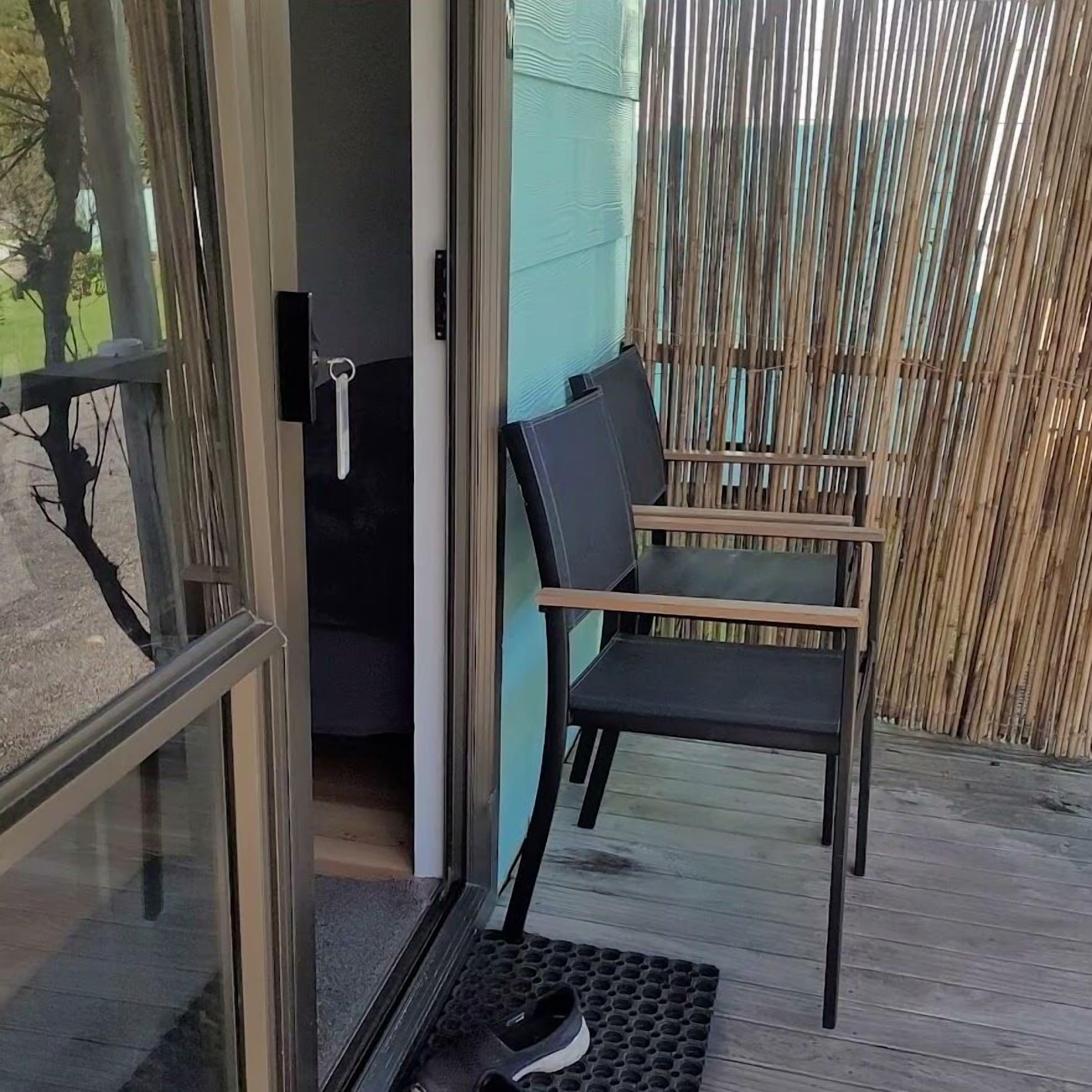 Una puerta de cristal que da a una habitación con una silla negra y una mesita.