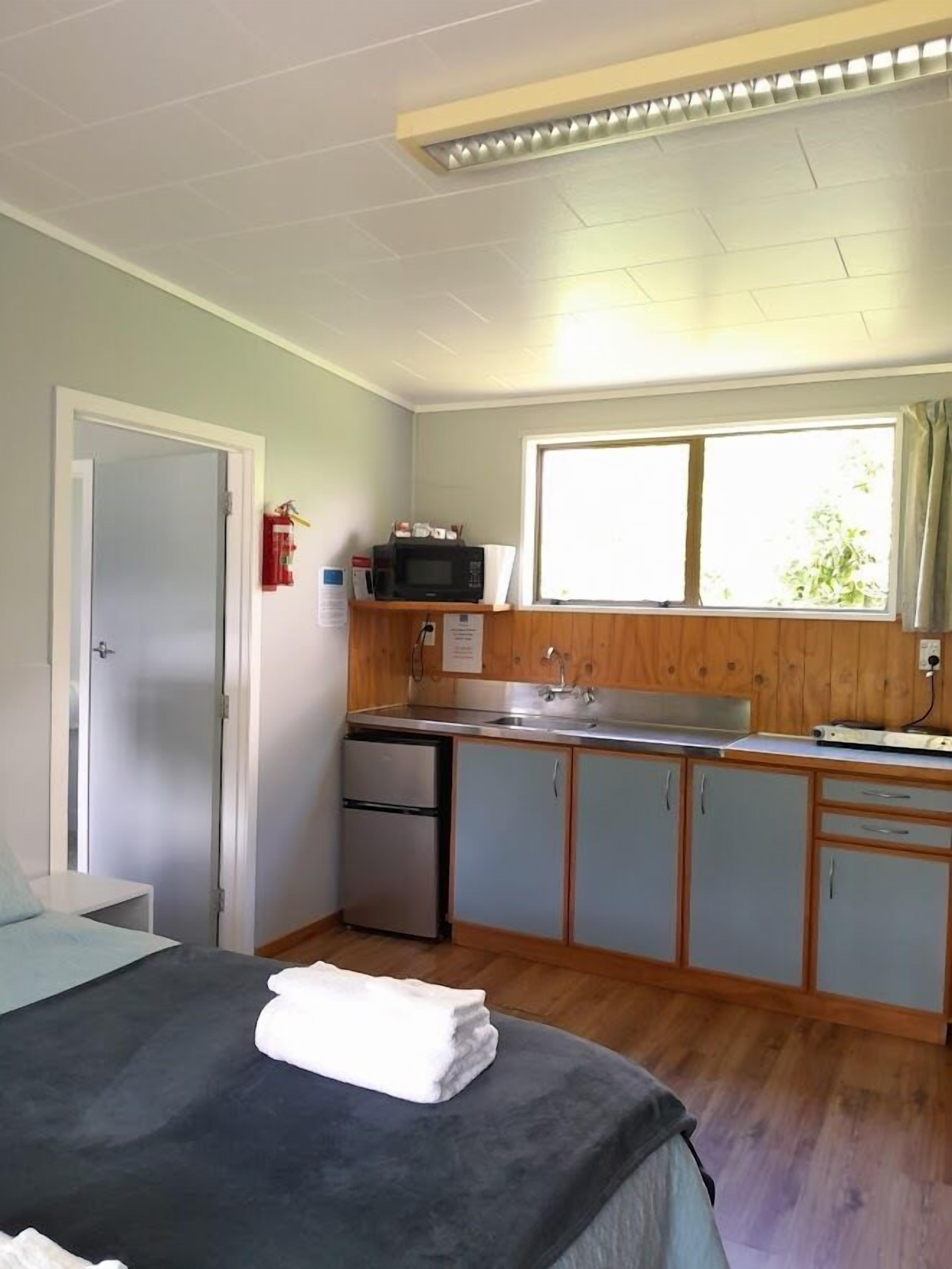 A compact room with a bed, a kitchenette, a window, and a door.