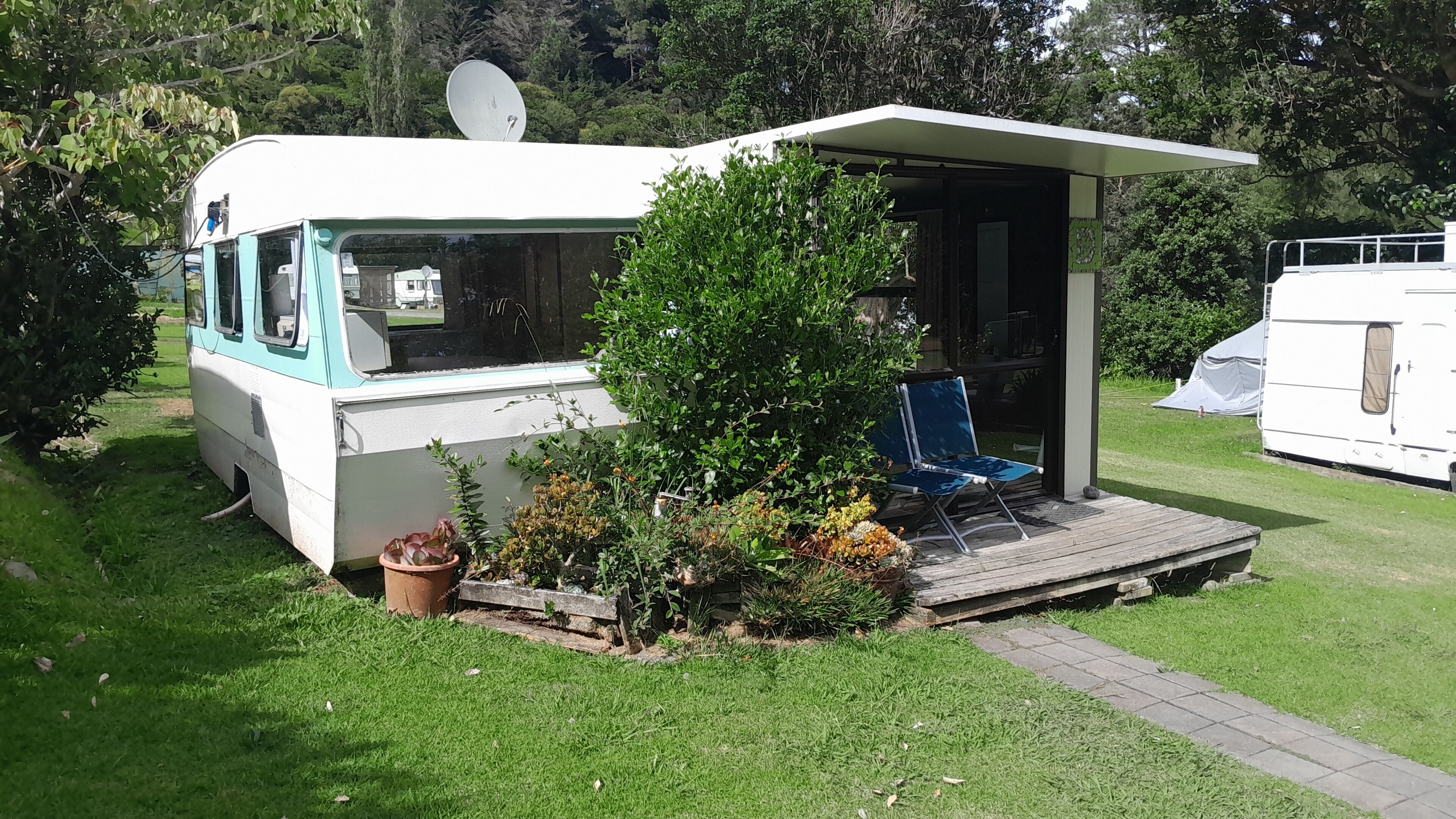 Una casa móvil con porche cubierto, antena parabólica y un pequeño jardín.