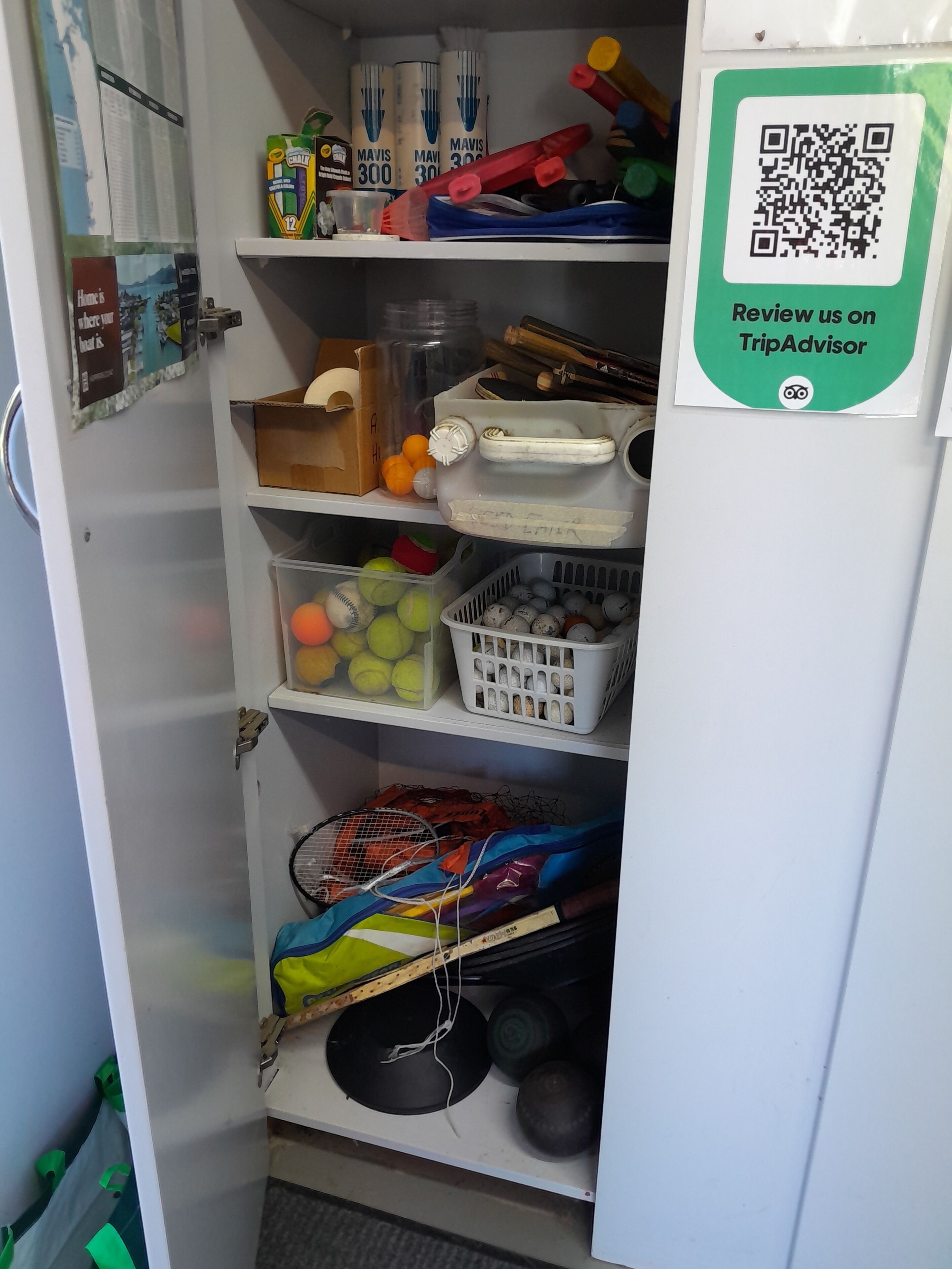 Ett förvaringsskåp med hyllor som innehåller sportutrustning, en QR-kod för recensioner på TripAdvisor och en skylt med ett meddelande.