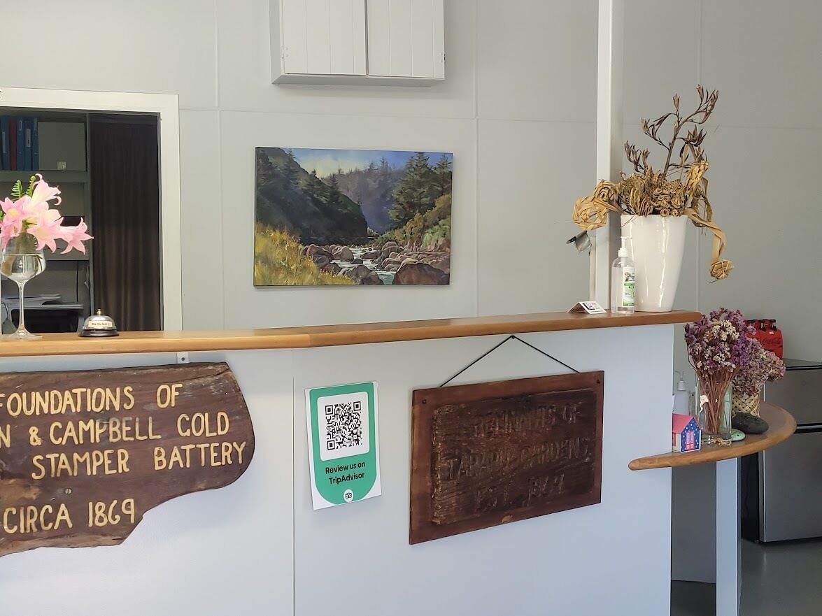 A reception desk with a sign about the foundations of Campbell Cold Stampers Battery circa 1869, a painting of a landscape, and a QR code for TripAdvisor.