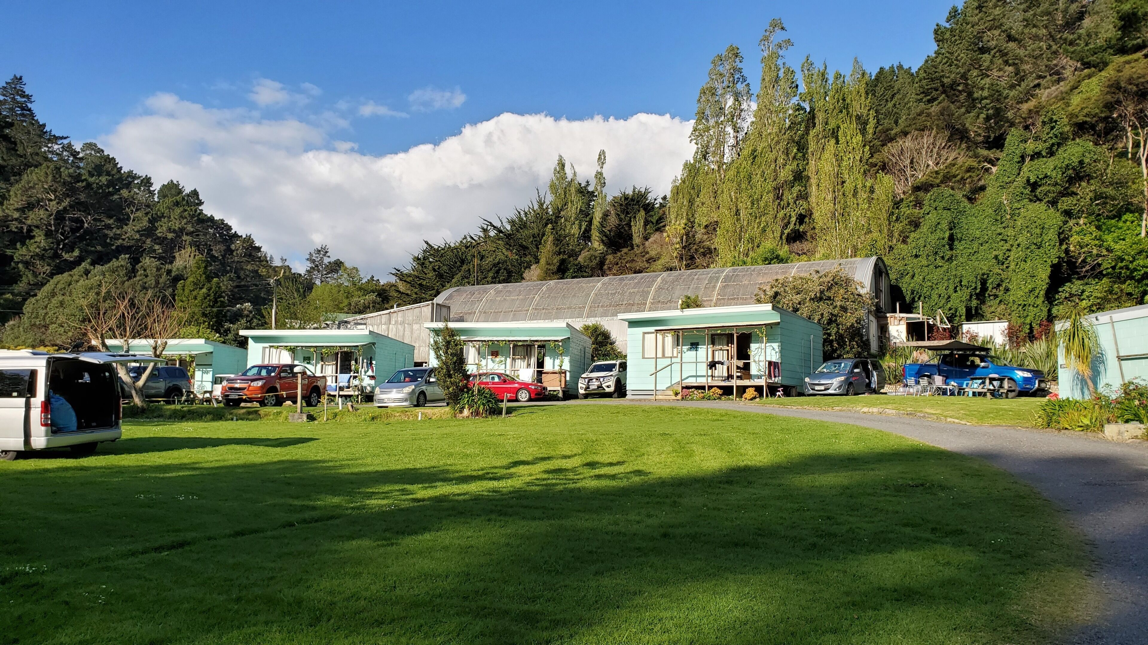 Un terrain de camping comprenant plusieurs mobil-homes, une zone herbeuse et une forêt en arrière-plan.