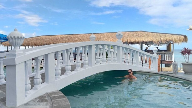 Une piscine à balustrade blanche, à l’eau claire, avec une structure à toit de chaume et une vue sur la mer.