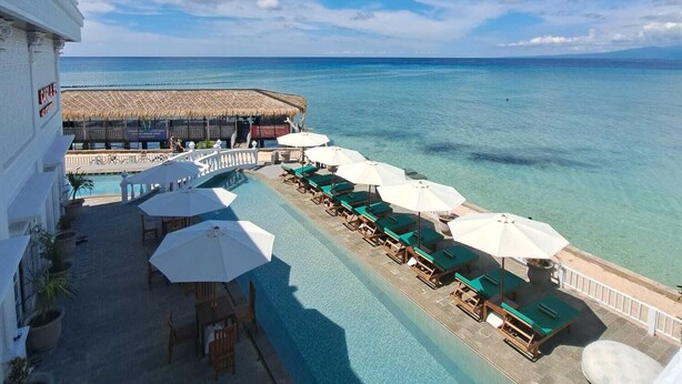 Zona de piscina en un resort con sillones de playa y sombrillas, con vista al océano.