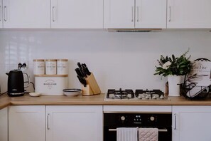 Eine Küche mit weißen Schränken, einer schwarzen Kaffeemaschine, einem Messerblock, einem Gasherd und einem Blumentopf.