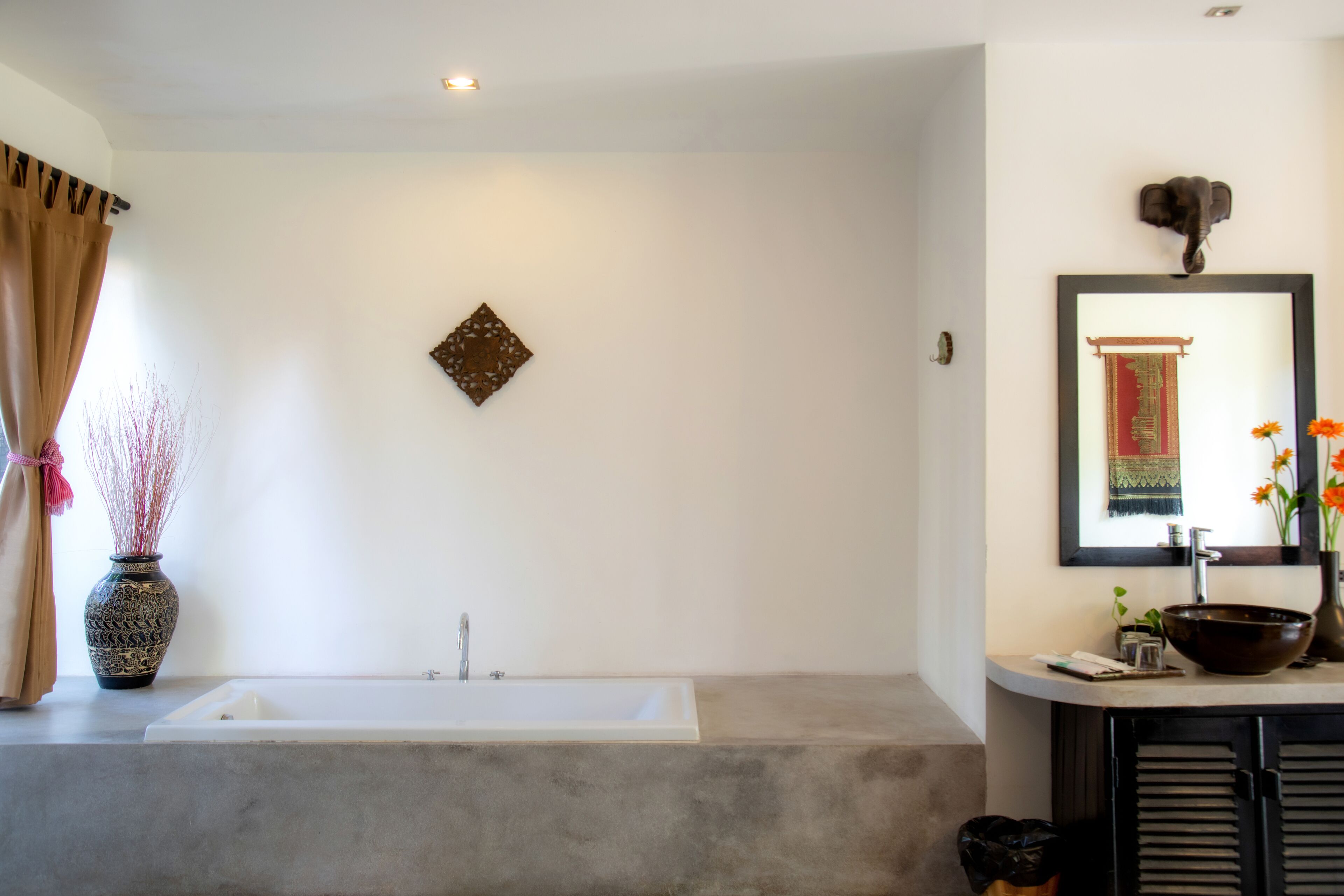 Une salle de bain avec une baignoire, un lavabo doté d’une grande cuve, un vase décoratif et un miroir fixé au mur.