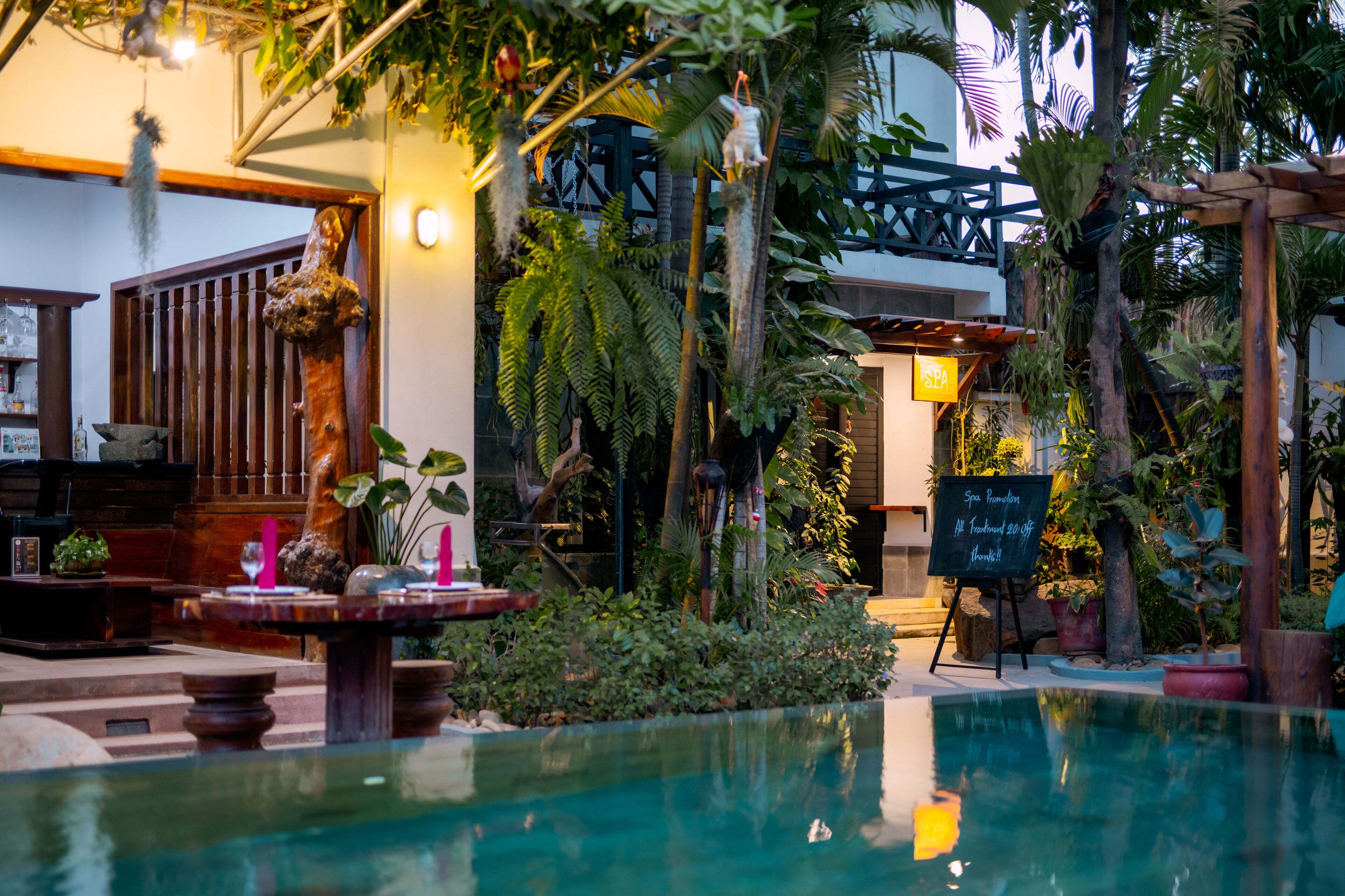 An indoor pool area with a wooden deck, a stone bench, and a signboard advertising spa treatments.