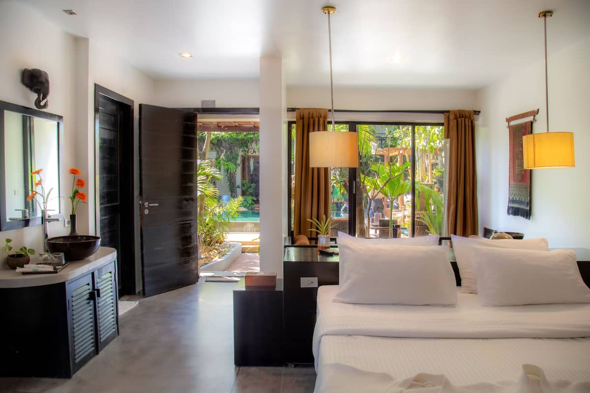A hotel room with a bed, bedside tables, a desk, a mirror, and a view of the garden.