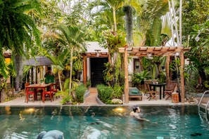 Relax in a serene pool area surrounded by lush tropical vegetation and a shaded pergola.