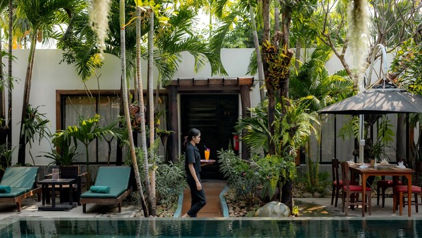 A pool area with lounge chairs, a table, and a covered seating area surrounded by tropical plants. - Bunwin Siem Reap (Siem Reap)