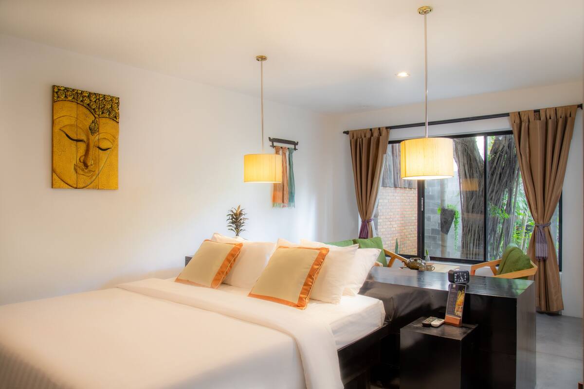 A hotel room with a bed, bedside table, lamp, and a window with curtains.