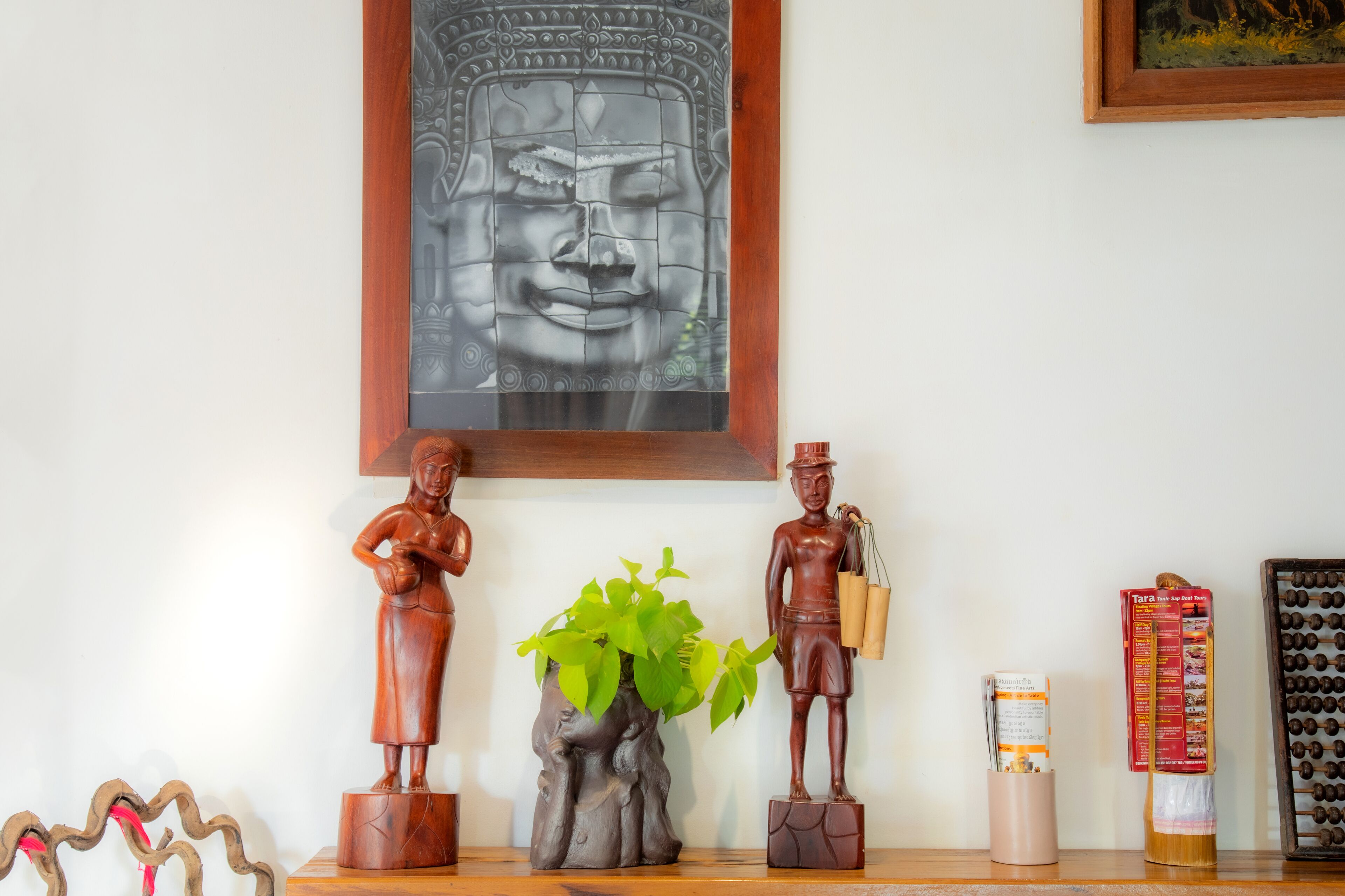 Una estantería de madera con diversos objetos, incluyendo una estatua de Buda, una planta pequeña, una figurita y un cuadro enmarcado.