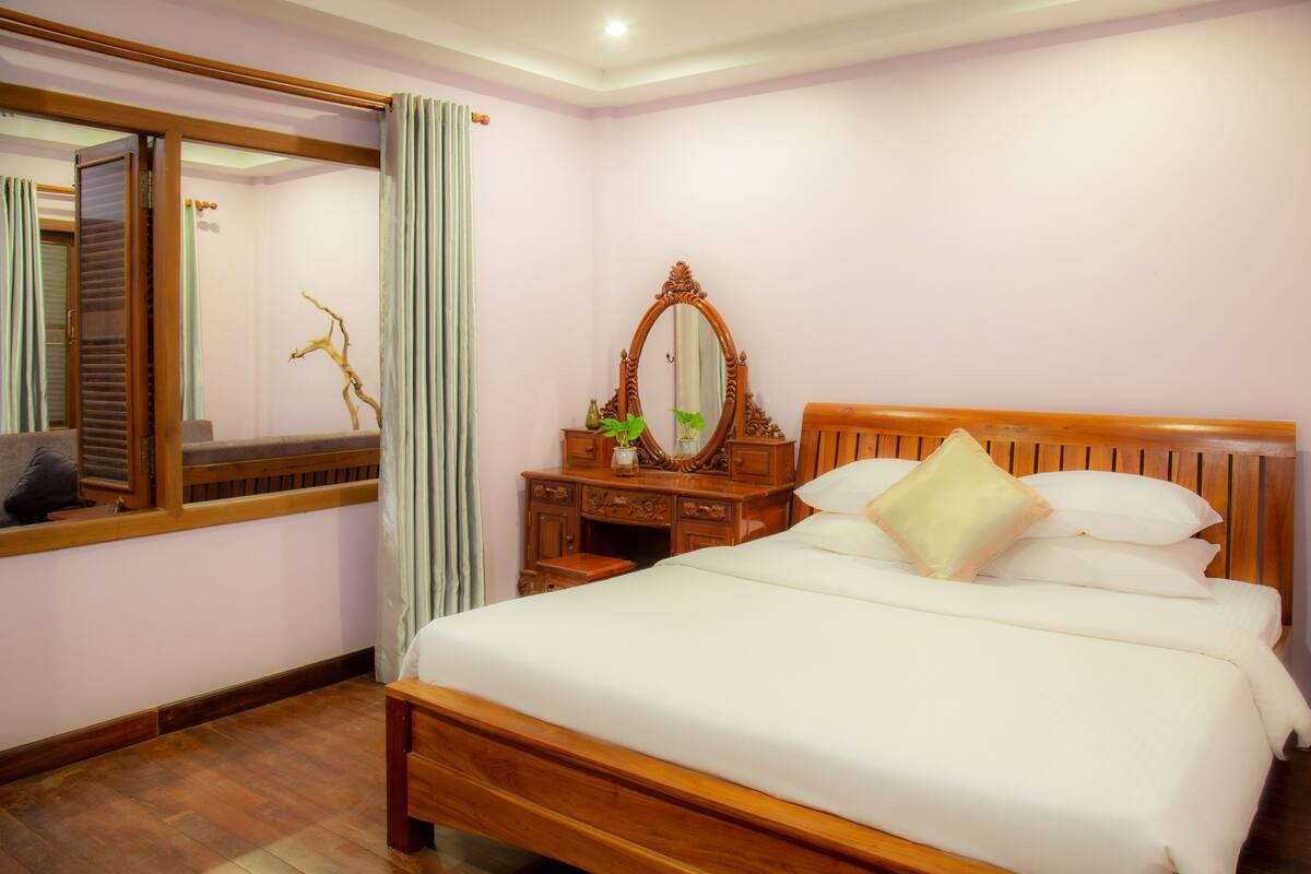 A bedroom with a wooden bed, a wooden dresser, a mirror, and a window with curtains.