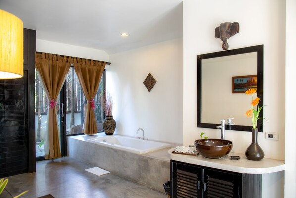 A modern bathroom with a large bathtub, a vanity with a bowl sink, a mirror, and a decorative elephant head.