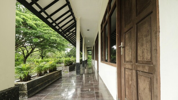 A corridor with a tiled floor, wooden doors, and a covered area with plants. - Hotel O Nyi Rindang Near Puskesmas Jekan Raya (Palangkaraya)