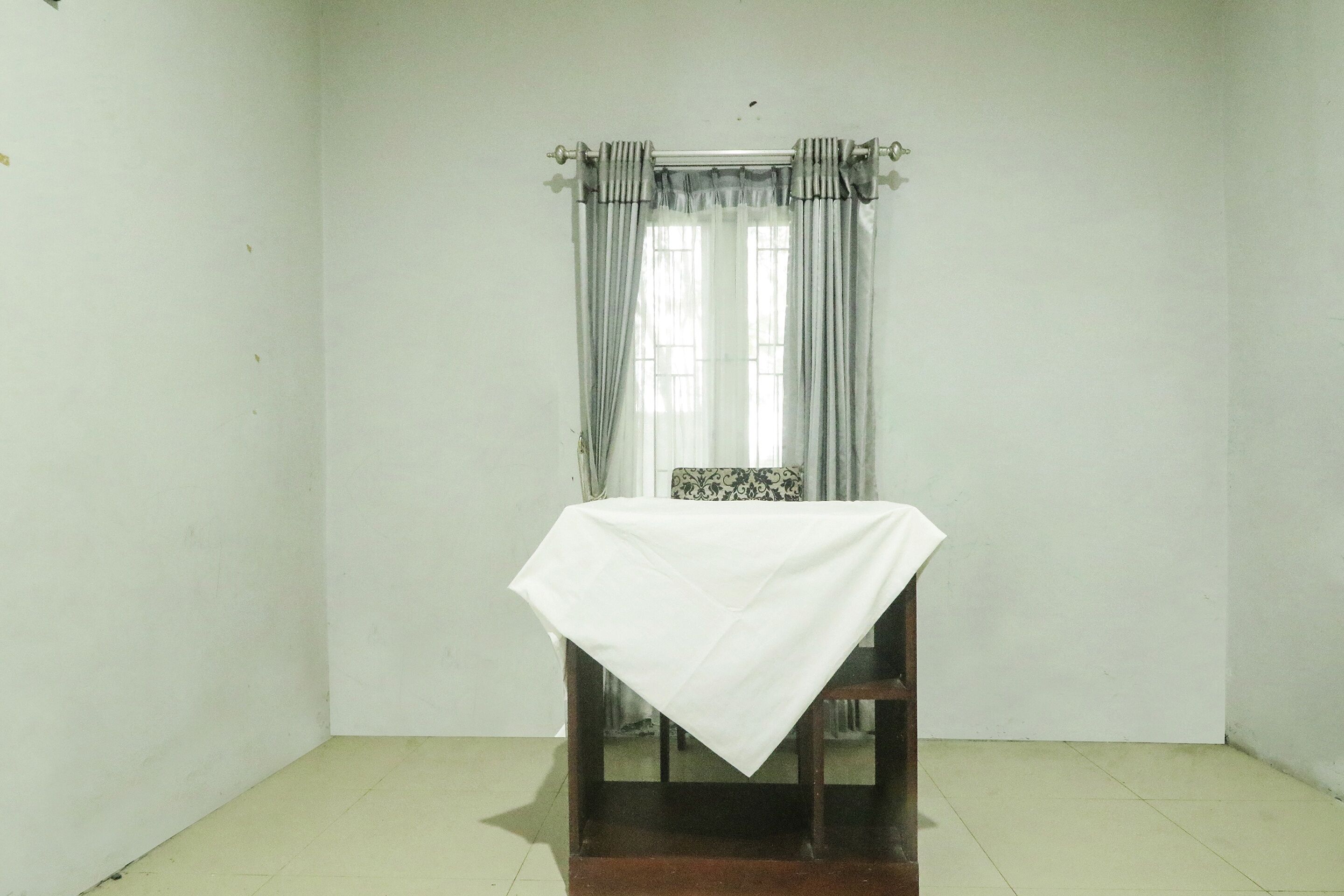 A room with a single table covered with a white cloth, a chair, and a window with curtains.