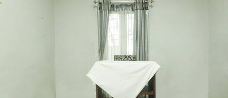 A room with a single table covered with a white cloth, a chair, and a window with curtains.