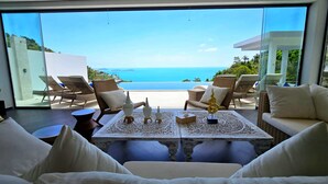 Habitación con vista al mar, amoblada con sofás y sillones blancos, y una mesa decorativa con una estatua dorada.