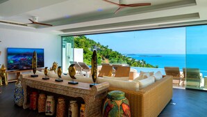 Una sala de estar moderna con un televisor grande, objetos decorativos y vistas al océano.