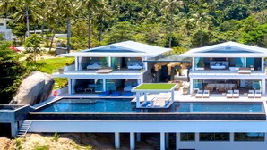 Una casa moderna de dos pisos con piscina, ventanas amplias y vistas al follaje circundante.