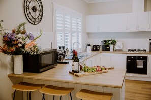 Een moderne keuken met witte kastjes, een magnetron, een fles wijn en een fruitschaal.