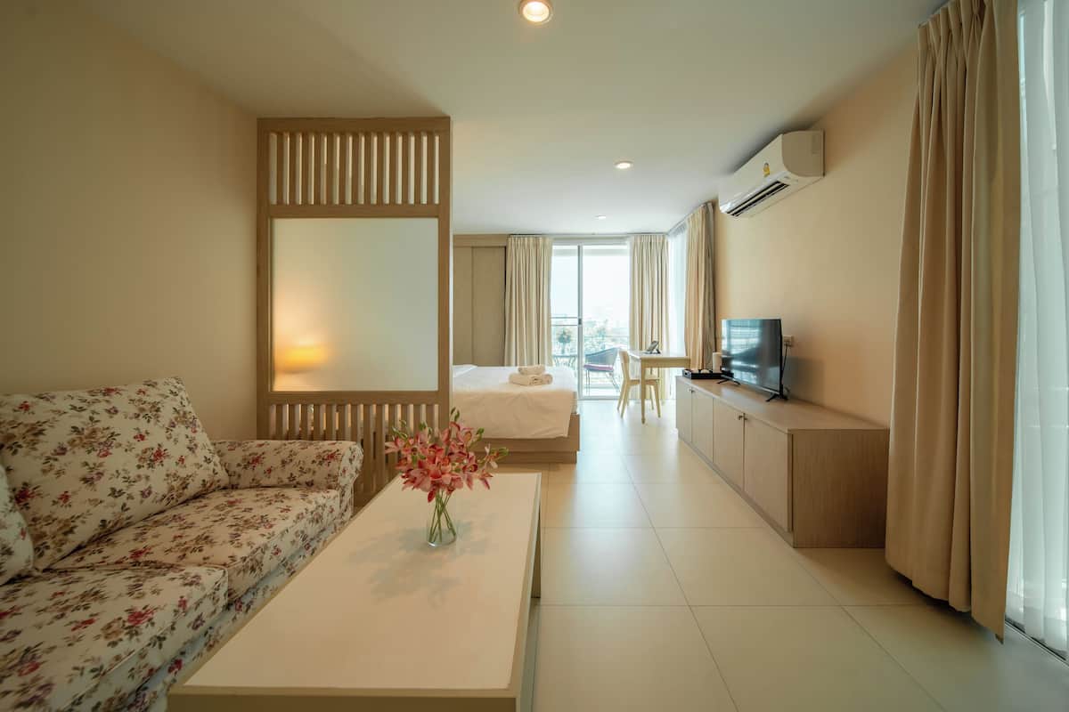 A hotel room with a sofa, a bed, a TV, a desk, and a view of the city.